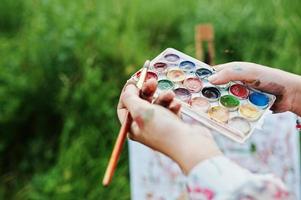 Nahaufnahme von weiblichen Händen, die Aquarellfarben und einen Pinsel halten, während sie in der Natur malen. foto