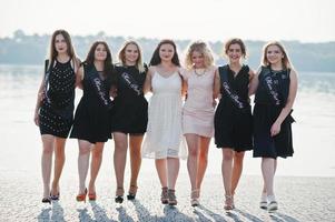 Gruppe von 7 Mädchen in Schwarz und 2 Bräute beim Junggesellinnenabschied am sonnigen Strand. foto