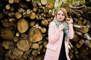 junges blondes mädchen im rosa mantel posierte vor holzstümpfen hintergrund. foto