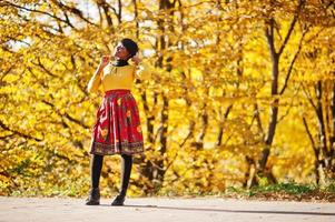 afroamerikanisches Mädchen im gelben und roten Kleid im goldenen Herbstpark. foto