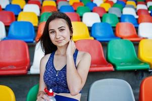 Porträt einer hübschen Frau in Sportkleidung, die im Stadion sitzt und Wasser trinkt. foto