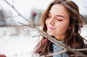 Nahaufnahme des Porträts eines sanften Mädchens in grauem Mantel in der Nähe der Äste eines schneebedeckten Baumes. foto