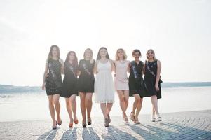 Gruppe von 7 Mädchen in Schwarz und 2 Bräute beim Junggesellinnenabschied am sonnigen Strand. foto