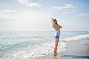 schönes modell, das sich an einem strand des meeres entspannt und auf jeansshorts, leopardenhemd und sonnenbrille trägt. foto