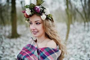 lockiges süßes blondes Mädchen mit Kranz im karierten Plaid am verschneiten Wald am Wintertag. foto