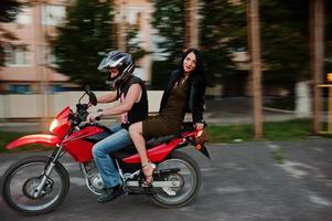 Frau in Kleid und Lederjacke, die mit einem anderen Mann Motorrad fährt. foto