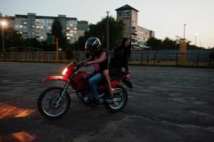 Frau in Kleid und Lederjacke, die mit einem anderen Mann Motorrad fährt. foto