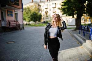 elegante blonde mädchen tragen eine schwarze lederjacke, die auf den straßen der stadt posiert. foto