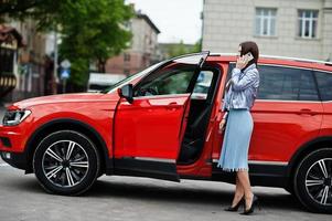 Outdoor-Foto einer wunderschönen Frau, die in der Nähe eines orangefarbenen SUV-Autos mit offener Tür posiert, sprechen Sie am Telefon. foto