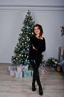 Mädchenabnutzung auf schwarzem Hintergrund Neujahrsbaum mit Geschenkboxen im Studio. frohes winterferienkonzept. foto