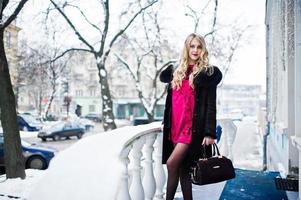 eleganz blondes mädchen in rotem abendkleid und pelzmantel auf den straßen der stadt im wintertag. foto