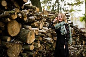 junges blondes Mädchen in Schwarz mit Schal posierte vor Holzstümpfen Hintergrund. foto