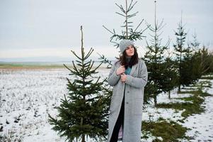 Porträt eines sanften Mädchens in grauem Mantel und Hut gegen den Neujahrsbaum im Freien. foto