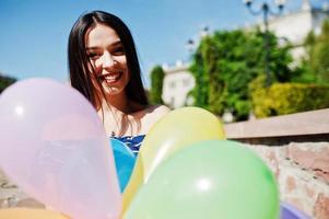 wunderschönes brünettes mädchen auf der straße der stadt mit luftballons an den händen. foto