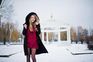 eleganz blondes mädchen im pelzmantel und im roten abendkleid posierte am verschneiten wintertag. foto