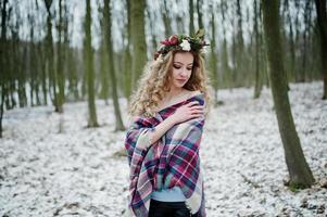 lockiges süßes blondes Mädchen mit Kranz im karierten Plaid am verschneiten Wald am Wintertag. foto