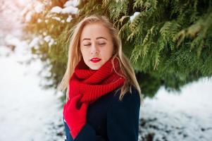 Blondes Mädchen in rotem Schal und Mantel, das am Wintertag im Park spazieren geht. foto