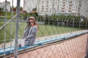 Mädchen im grauen Mantel mit Sonnenbrille im kleinen Straßenstadion. foto