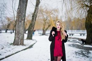 eleganz blondes mädchen im pelzmantel und im roten abendkleid posierte am verschneiten wintertag. foto