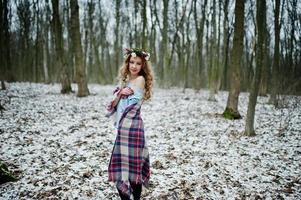 lockiges süßes blondes Mädchen mit Kranz im karierten Plaid am verschneiten Wald am Wintertag. foto