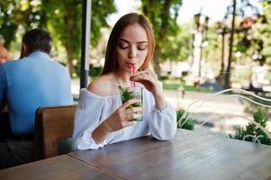 Porträt einer atemberaubenden jungen Frau, die Mojito-Cocktail im Café neben dem Park trinkt. foto