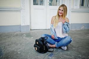 blonde Mädchen tragen Jeans mit Rucksack gegen alte Tür gestellt. foto