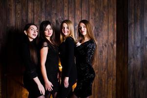vier süße freundinnen tragen schwarze kleider gegen große leichte weihnachtssterndekoration auf hölzernem hintergrund. foto