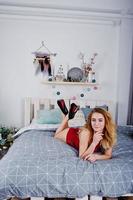 sexy blondes Model in roten Dessous und High Heels auf dem Bett gegen Neujahrsbaum. foto