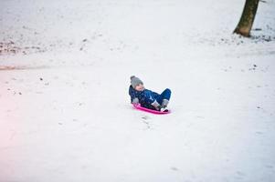 süßes kleines Mädchen mit Untertassenschlitten im Freien am Wintertag. foto