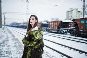 brünettes mädchen im grünen pelzmantel auf der bahnsteigstation am wintertag. foto