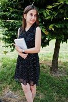 Porträt einer schüchternen jungen Frau in schwarzem Tupfenkleid, das Bücher im Park hält. foto
