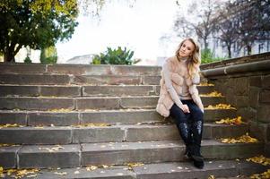 blondes mädchen im pelzmantel und brille, die auf treppen mit gelben blättern sitzen. foto