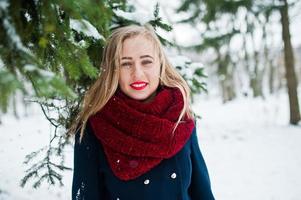 Blondes Mädchen in rotem Schal und Mantel, das am Wintertag im Park spazieren geht. foto