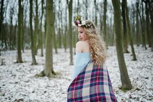 lockiges süßes blondes Mädchen mit Kranz im karierten Plaid am verschneiten Wald am Wintertag. foto