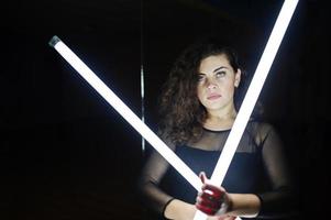 lockiges brünettes plus-size-model mit zwei langen led-lampen im tanzraum mit spiegel. foto