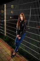 Nachtporträt von Mädchen Model Wear auf Jeans und Lederjacke gegen Eisenzaun. foto