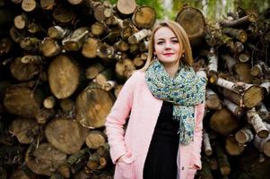 junges blondes mädchen im rosa mantel posierte vor holzstümpfen hintergrund. foto