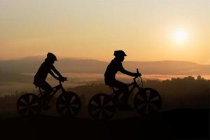 Silhouetten Mann und Fahrrad auf dem Berg im Sonnenlicht foto