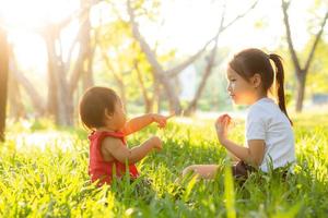 schönes junges asiatisches kind, das im sommer im park spielt, genießt und fröhlich auf grünem gras, kinderaktivitäten mit entspanntheit und glück zusammen auf wiese, familien- und urlaubskonzept. foto