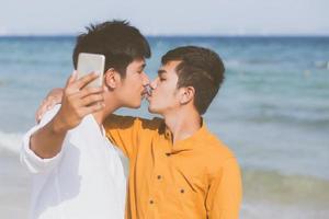 junges paar des homosexuellen porträts, das ein selfie-foto zusammen mit intelligentem handy am strand macht, homosexueller lgbt-liebhaber mit kuss im urlaub auf meer, zwei mann, der reisen wird, urlaubskonzept. foto