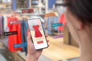 Einkaufen mit Smartphone und Augmented-Reality-App im Boutique-Konzept. Anprobieren der neuesten Kleidung in verschiedenen Größen und Farben. Frau mit Smartphone foto