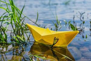 gelbes Papierboot auf Grund in der Nähe des Flussufers im Gras foto