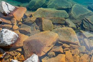 schöne Küstensteine in Türkis- und Orangefarben, die teilweise unter dem klaren Süßwasser des Sees liegen foto