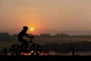 Silhouetten Mann und Fahrrad auf dem Berg im Sonnenlicht foto