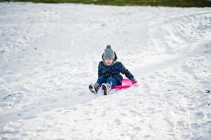 süßes kleines Mädchen mit Untertassenschlitten im Freien am Wintertag. foto