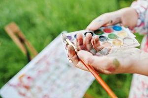 Nahaufnahme von weiblichen Händen, die Aquarellfarben und einen Pinsel halten, während sie in der Natur malen. foto