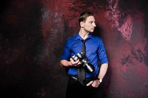 studioporträt eines stilvollen professionellen fotografenmannes mit kamera, tragen auf blauem hemd und krawatte. foto