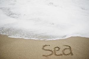 Nahaufnahmefoto des Sandaufschriftmeeres durch die schäumenden Wellen. foto
