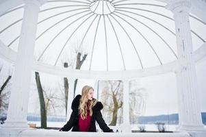 eleganz blondes mädchen im pelzmantel und im roten abendkleid posierte am verschneiten wintertag. foto