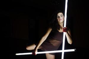 lockiges brünettes plus-size-model mit zwei langen led-lampen im schwarzen raum. foto